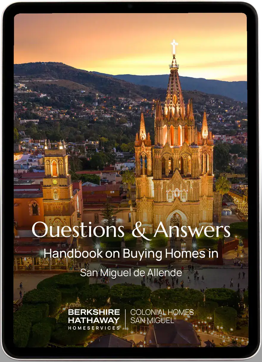 Evening view of San Miguel de Allende with the illuminated Parroquia church and promotional text for Berkshire Hathaway HomeServices Luxury Collection and a housing handbook.
