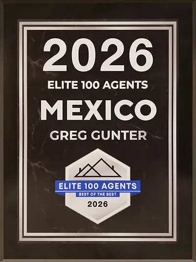 Framed award poster reading '2026 Elite 100 Agents Mexico Greg Gunter' with a mountain logo and a blue-bordered 'Elite 100 Agents Best of the Best 2026' badge.