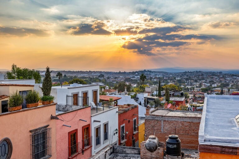 Sunset over a colorful Mediterranean neighborhood with terracotta rooftops and sunbeams breaking through clouds onto the city below