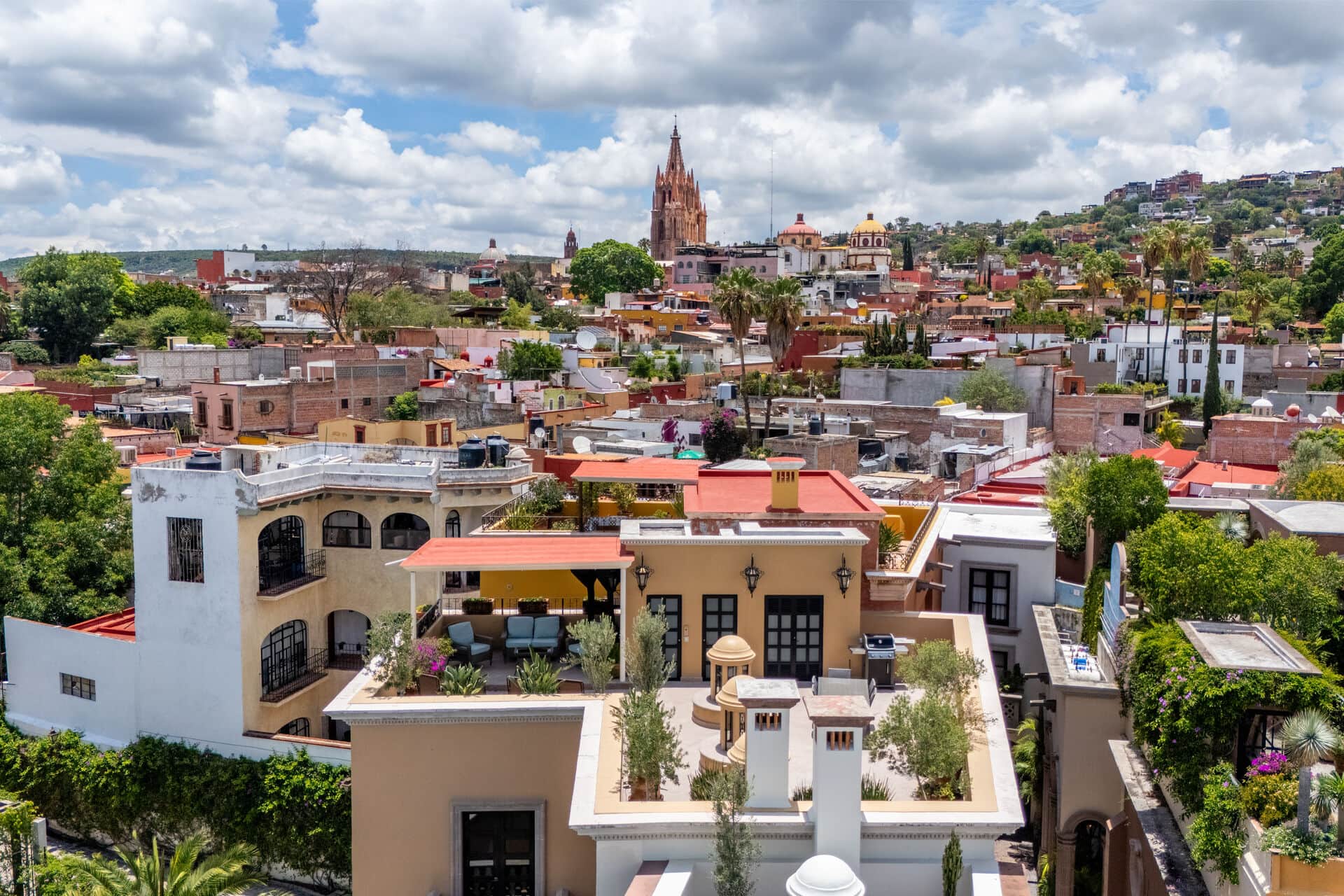 Panoramic view of a colorful Mexican town with a tall cathedral spire, domed churches, and clustered houses under a cloudy sky.