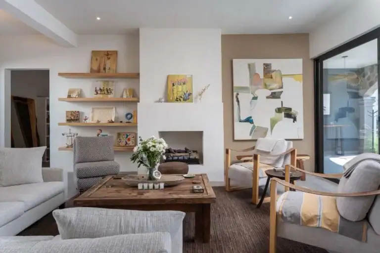Bright, contemporary living room with a white fireplace, open shelves, abstract art, and beige seating around a rustic wooden coffee table, San Miguel de Allende