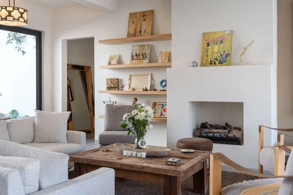 Bright, modern living room with a gray sofa, wooden coffee table, built‑in fireplace, and open shelves displaying art and books, San Miguel de Allende