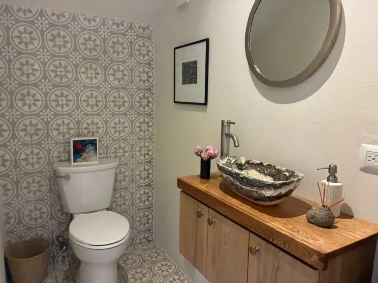 Bathroom with patterned gray tile, white toilet, and a wicker basket on the floor next to it, San Miguel de Allende