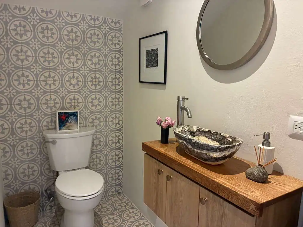Bathroom with patterned gray tile, white toilet, and a wicker basket on the floor next to it, San Miguel de Allende