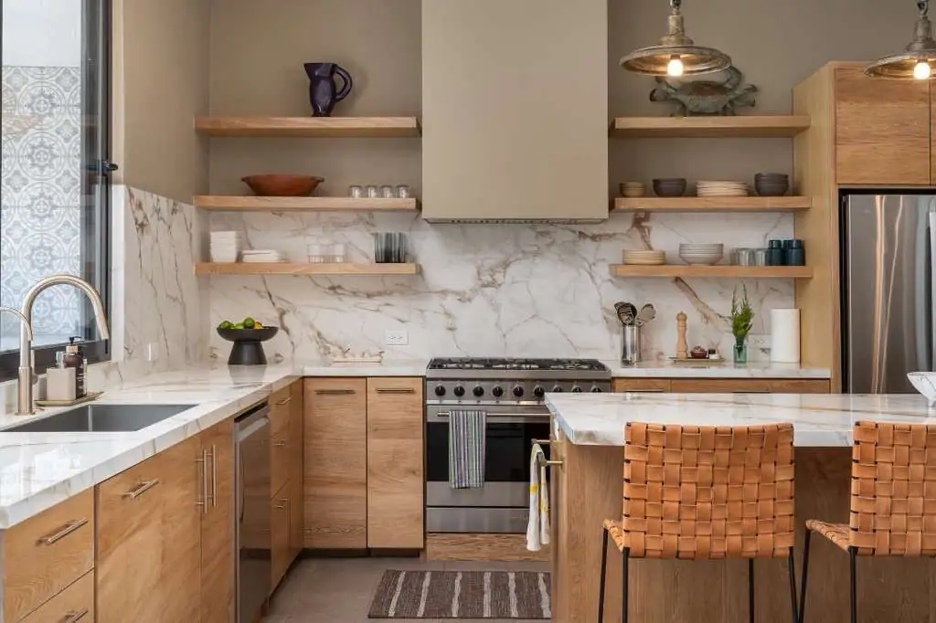 Modern kitchen with marble backsplash and countertops, wooden cabinets, open shelves, and a marble island with woven bar stools, San Miguel de Allende