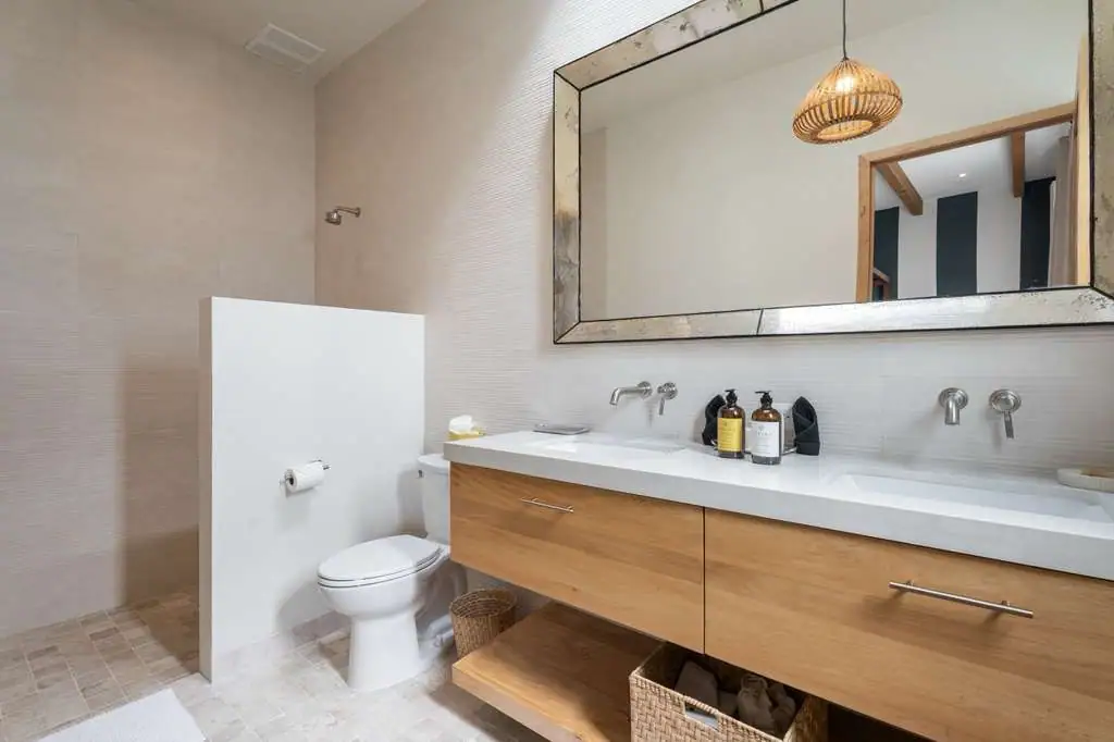 Modern bathroom with a double-sink wooden vanity, large framed mirror, and toilet on the left, San Miguel de Allende
