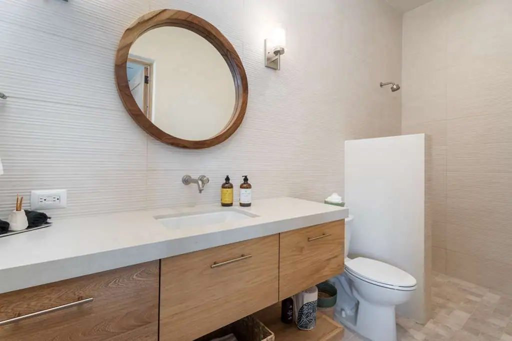 Modern bathroom with a wooden vanity, round wood-framed mirror, and two soap bottles on the counter next to a sink, San Miguel de Allende