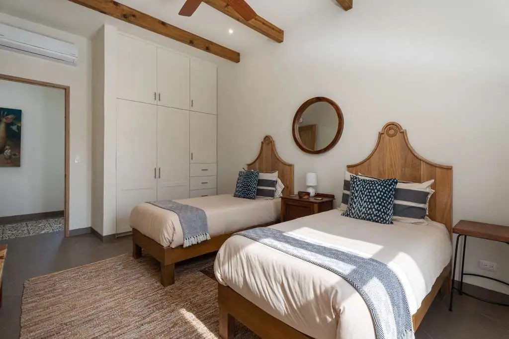 Bedroom with two single beds, light bedding, wooden headboards, a round mirror above a shared nightstand, and a tall white wardrobe to the left, San Miguel de Allende