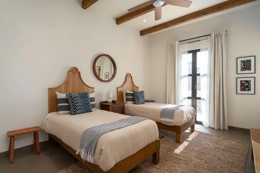 Twin bedroom with wood headboards, matching nightstand, round mirror, and ceiling beams in a bright room, San Miguel de Allende