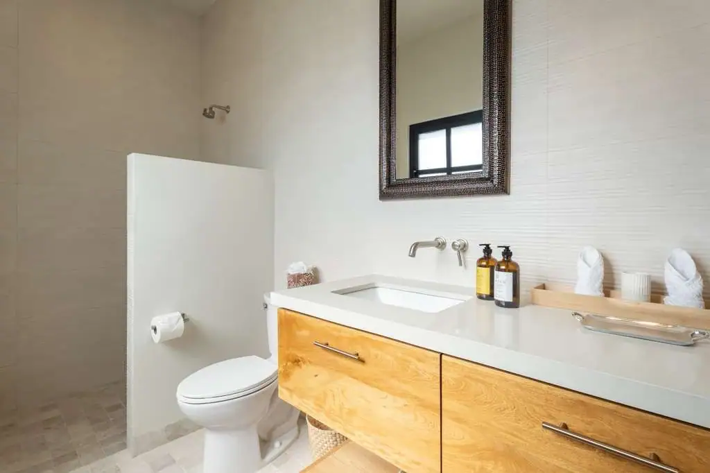 Contemporary bathroom with a white countertop sink, wooden vanity, and a framed mirror above; toiletries on the counter, San Miguel de Allende