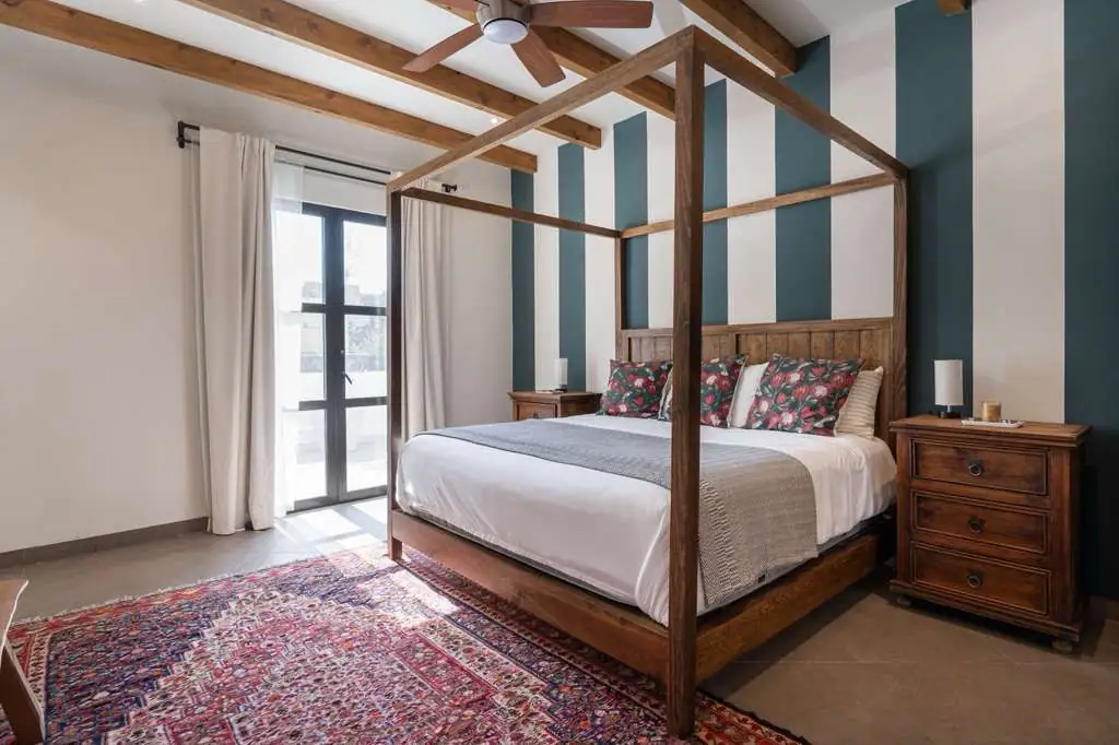 Wood four-poster bed with white linens and floral pillows in a bedroom with blue striped accent walls and two wooden nightstands at the sides, San Miguel de Allende