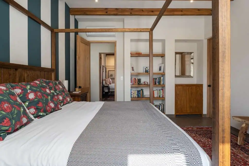 Wooden four-poster bed in a bright bedroom with a blue striped accent wall and built-in bookshelves nearby, San Miguel de Allende
