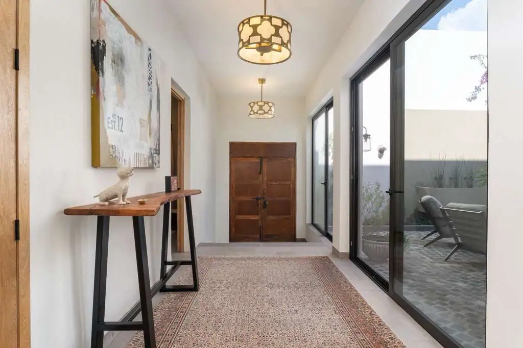 Narrow entry hall with a wooden console table, cat sculpture, abstract art, and glass doors to an outdoor patio, San Miguel de Allende