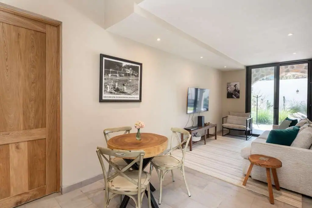Open-plan living and dining area with a round wooden table and four metal chairs, beige sofa, and glass doors to a garden outdoor, San Miguel de Allende
