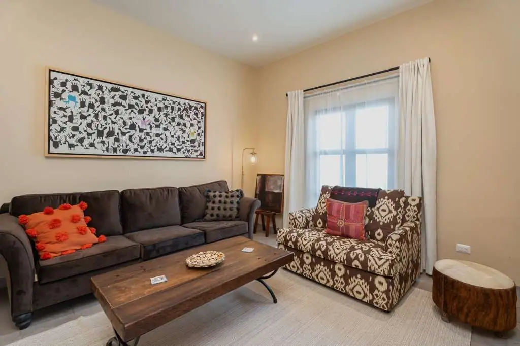 Cozy living room with a dark gray sectional, patterned armchair, wooden coffee table, and abstract wall art, San Miguel de Allende