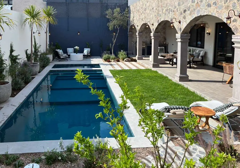 Outdoor backyard with a rectangular pool, stone arches, and a seating area on a sunny patio, San Miguel de Allende