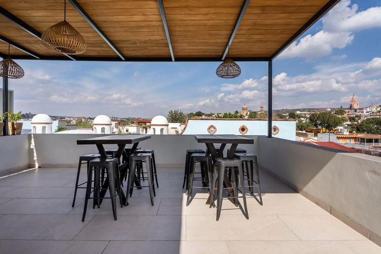 Rooftop patio with two high black tables and stools, overlooking a city with white domed buildings under a blue sky, San Miguel de Allende