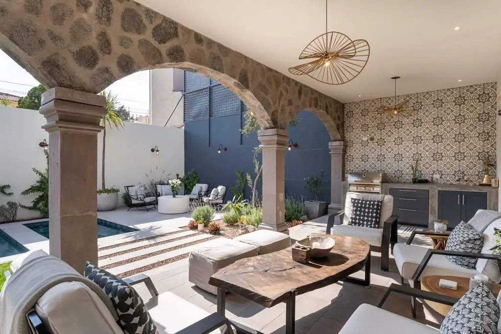 Outdoor covered patio with stone arches and a seating area around a live-edge wooden table, overlooking a small pool and garden, San Miguel de Allende