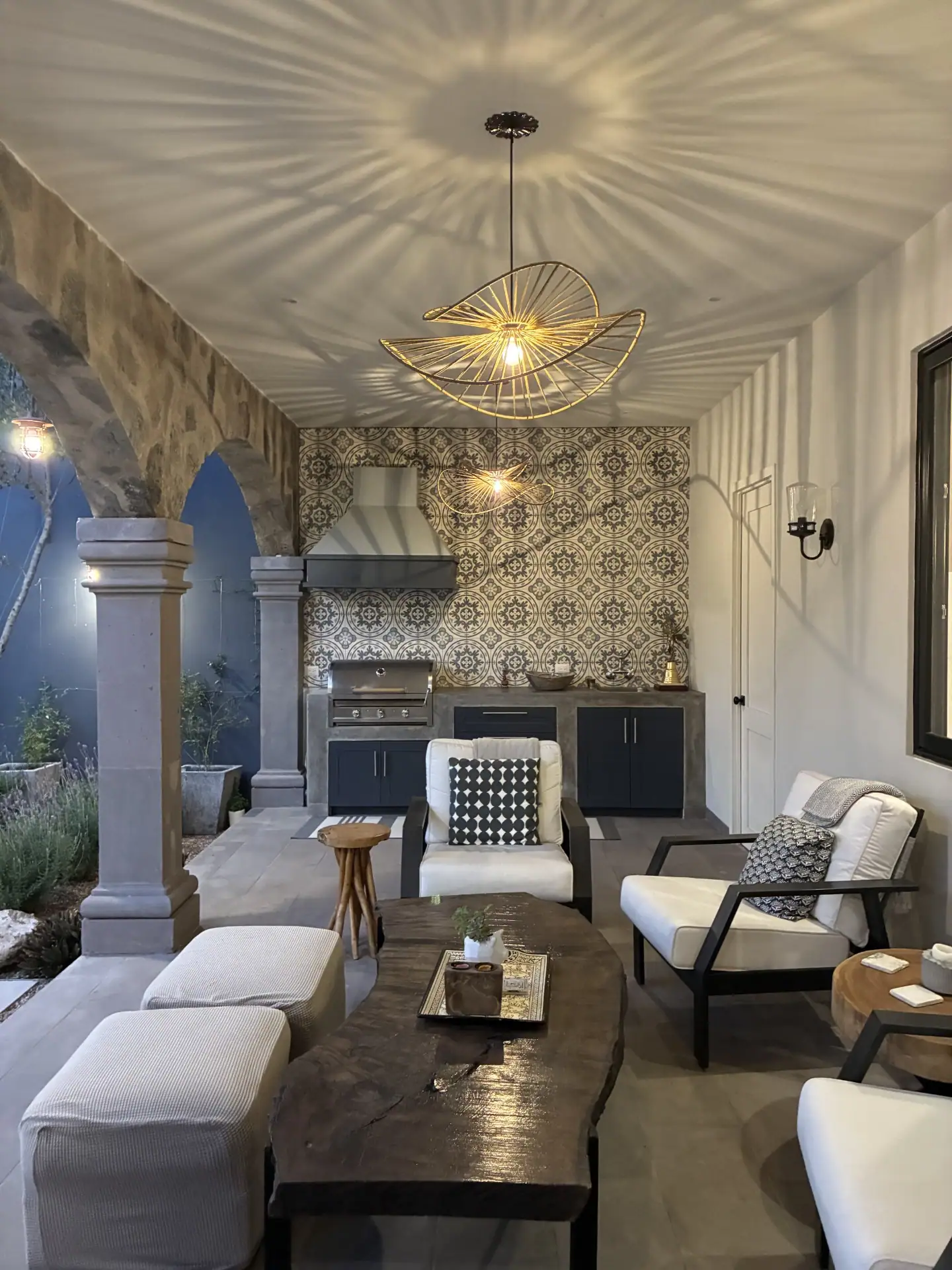 Covered outdoor patio with stone arches, built-in grill, and a patterned tile backsplash; a sculptural wire pendant light casts radial shadows on the ceiling, San Miguel de Allende