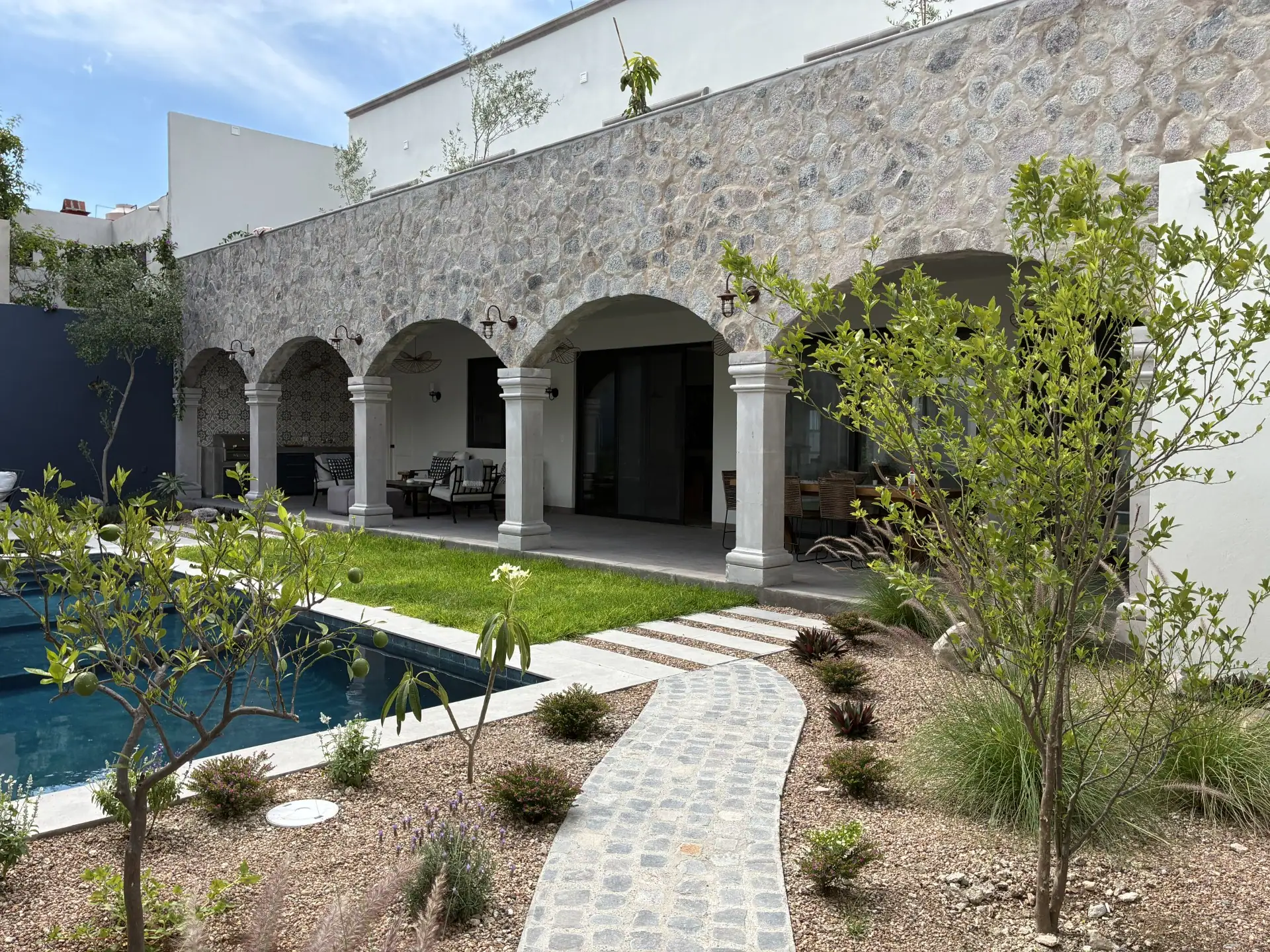Stone-walled courtyard with arched colonnade and outdoor seating under arches, next to a rectangular pool and landscaped garden, San Miguel de Allende