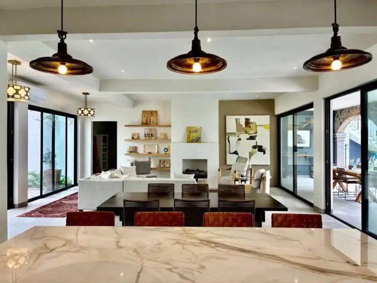 Open-concept living and dining area with a marble kitchen island in the foreground, dark wood chairs, and a white sofa beyond, San Miguel de Allende