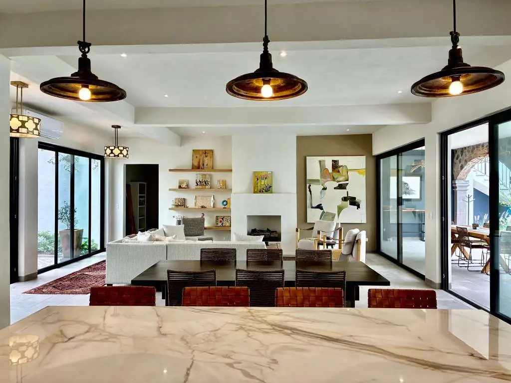 Open-concept living and dining area with a marble kitchen island in the foreground, dark wood chairs, and a white sofa beyond, San Miguel de Allende