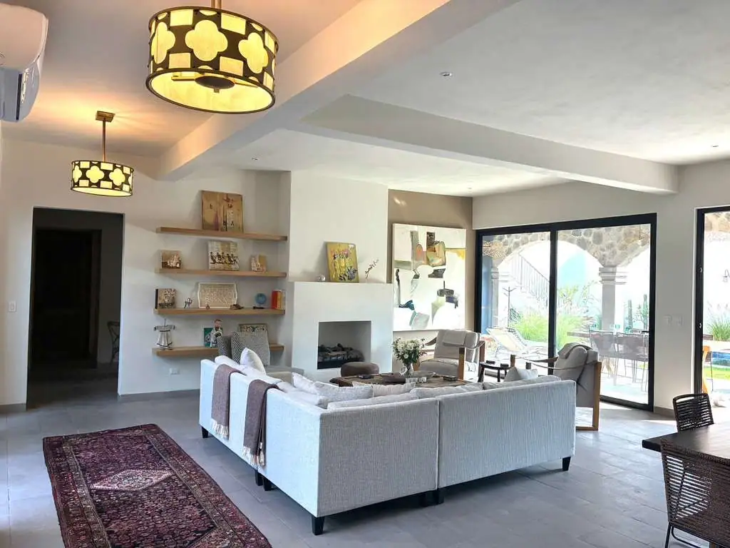 Open-concept living room with a gray L-shaped sofa, built-in shelves, and a white fireplace, plus pendant lights and large sliding doors to the patio, San Miguel de Allende