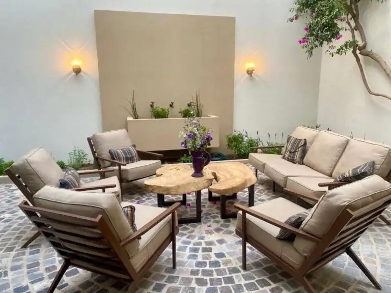 Outdoor patio seating arranged in a circular lounge with beige cushioned chairs and a wooden coffee table, purple vase centerpiece, and greenery surrounding, San Miguel de Allende