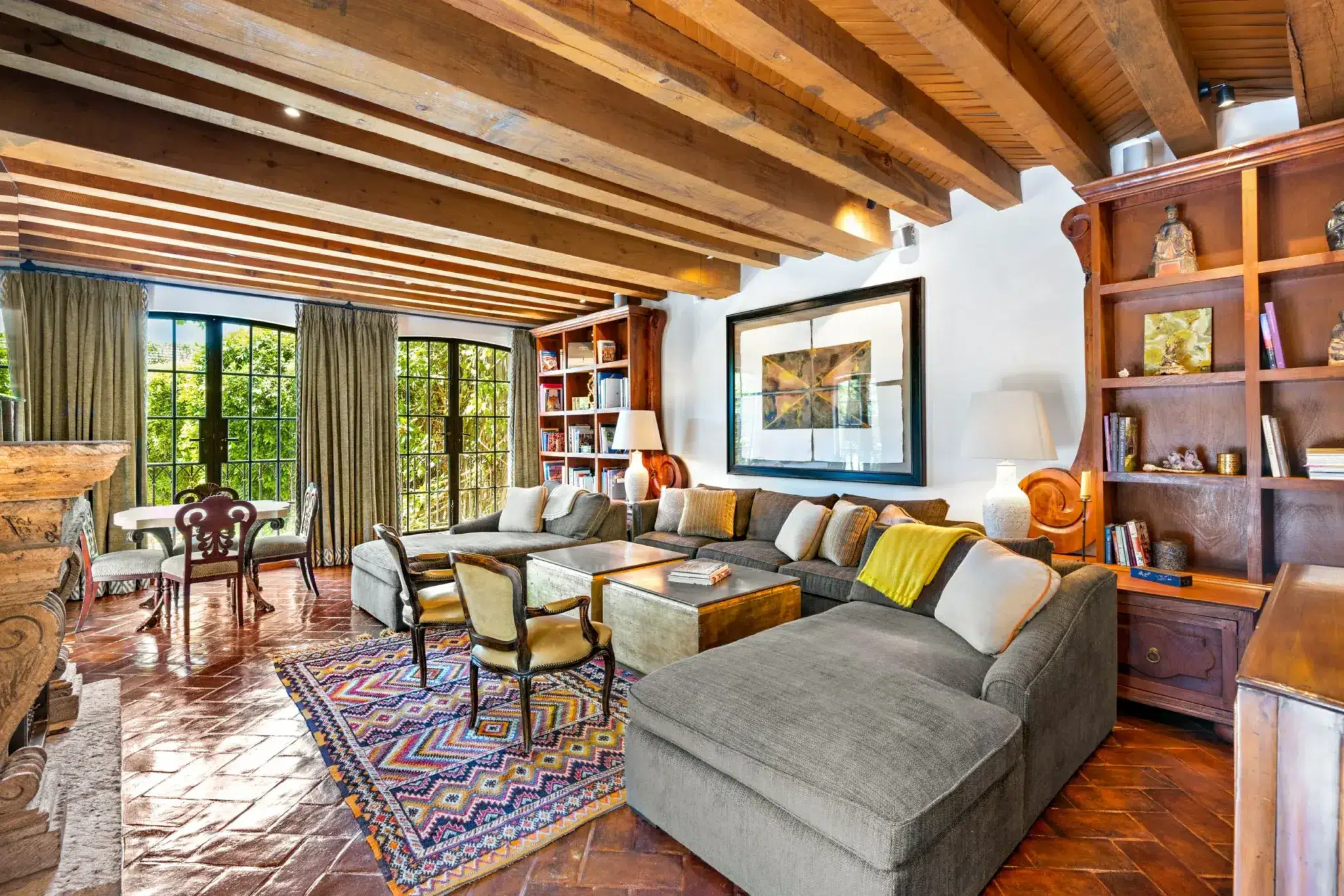 Cozy living room with exposed wooden beam ceiling, large grid windows, and a gray sectional sofa, San Miguel de Allende