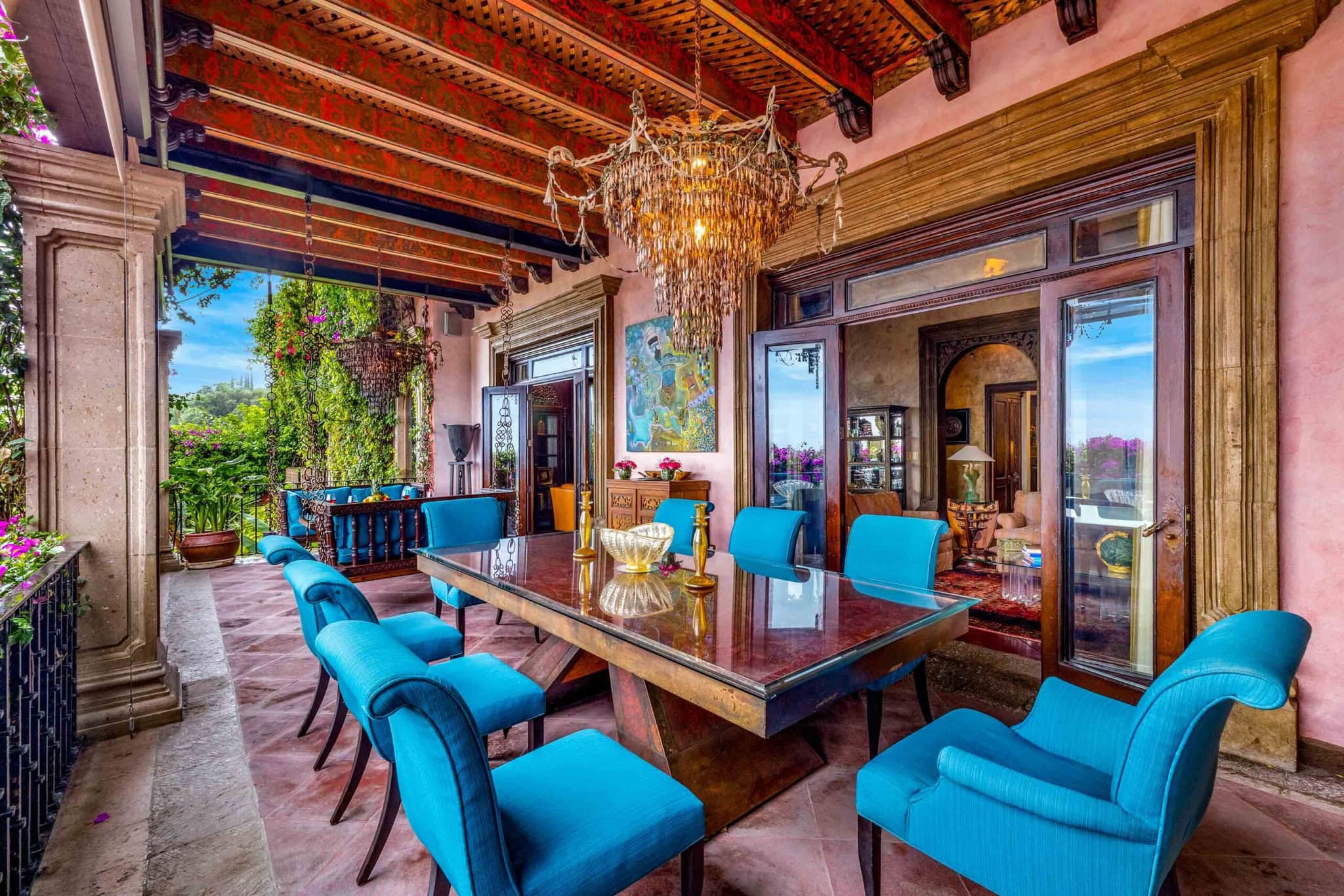 Luxurious outdoor dining area with turquoise chairs around a glass table under a crystal chandelier on a pink-walled veranda, San Miguel de Allende