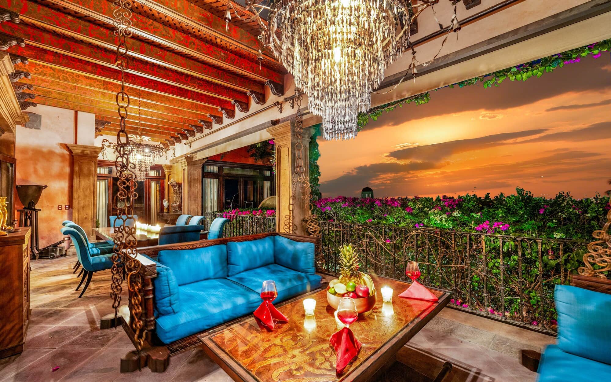 Luxurious outdoor terrace at sunset with blue cushioned seating, ornate chandeliers, and a garden railing full of flowers, San Miguel de Allende