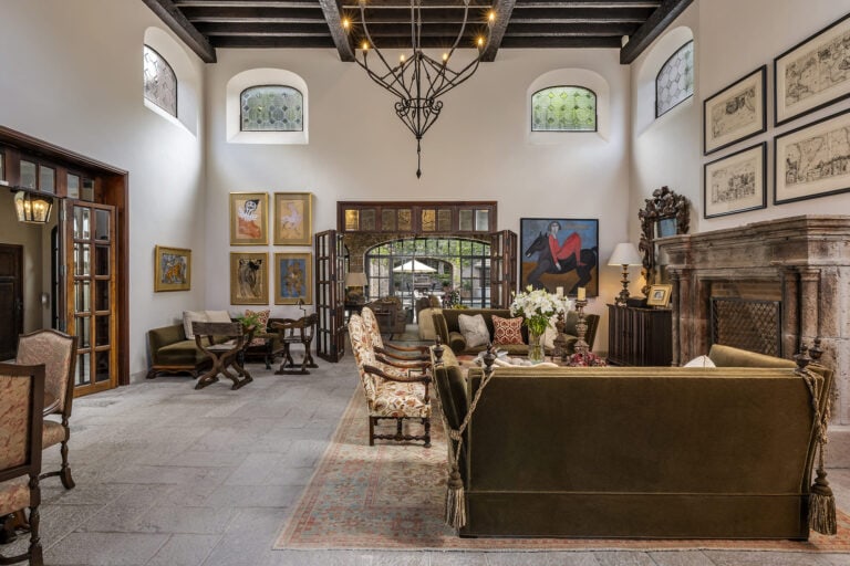 Luxurious living room lobby with antique furniture, a metal chandelier, and a stone fireplace. Open double doors lead to an outdoor courtyard, San Miguel de Allende