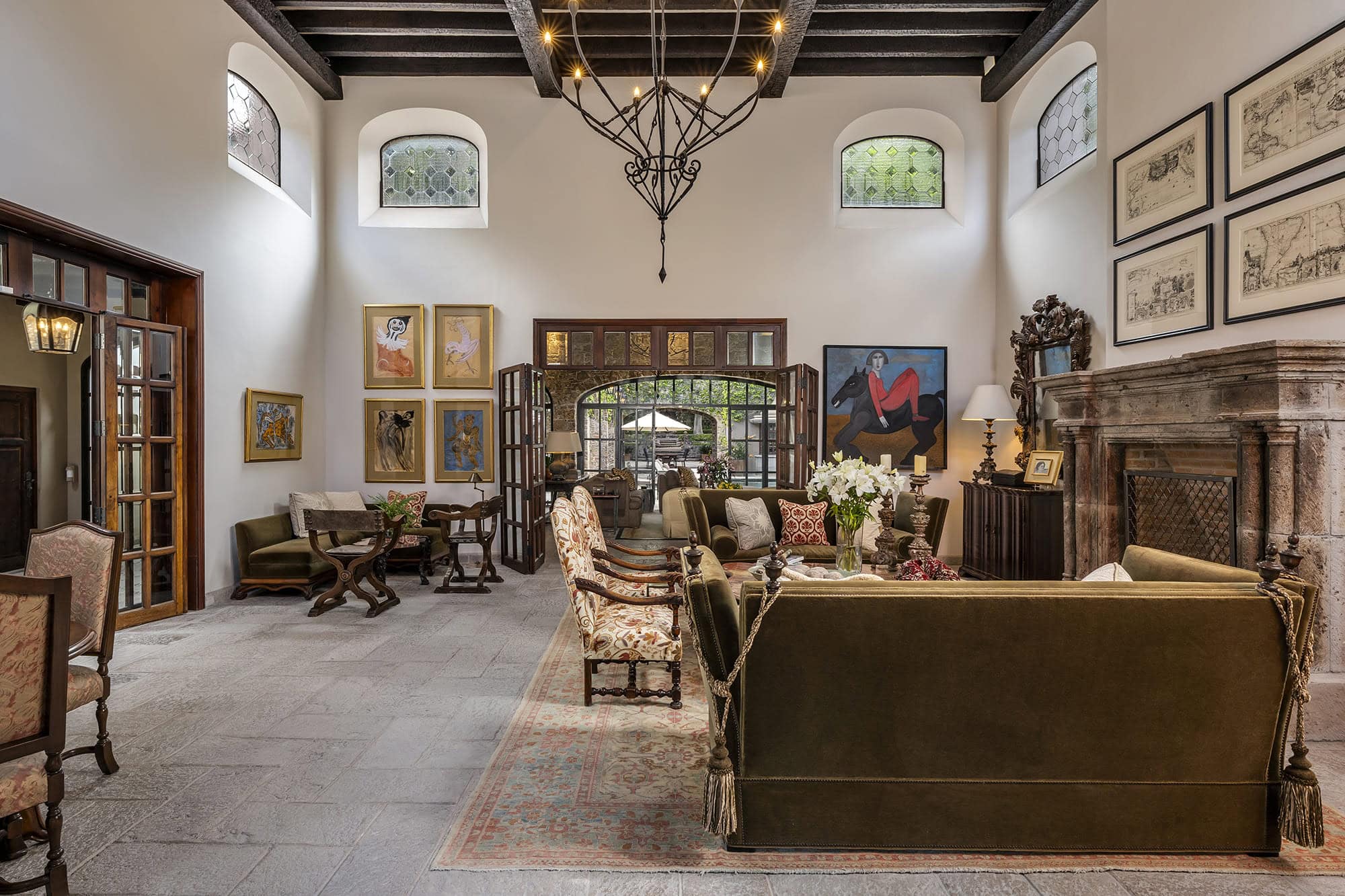 Luxurious living room lobby with antique furniture, a metal chandelier, and a stone fireplace. Open double doors lead to an outdoor courtyard, San Miguel de Allende