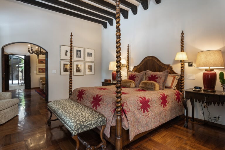 Luxurious bedroom featuring a dark wood four-poster bed with patterned red bedding and a tufted bench at the foot, San Miguel de Allende
