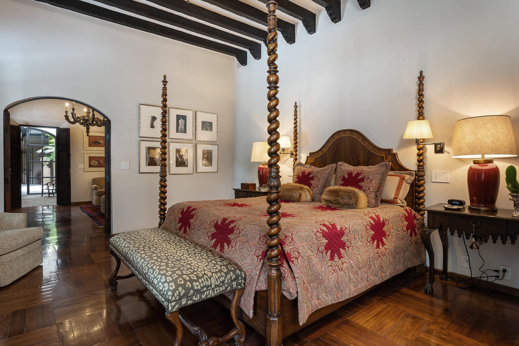 Luxurious bedroom featuring a dark wood four-poster bed with patterned red bedding and a tufted bench at the foot, San Miguel de Allende