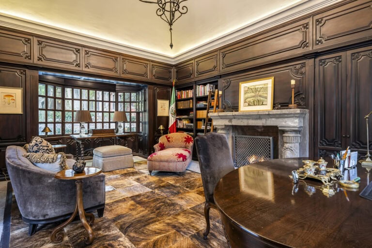 Luxurious dark wood-paneled living room with a marble fireplace, built-in bookshelves, and a round wooden table with chairs, San Miguel de Allende