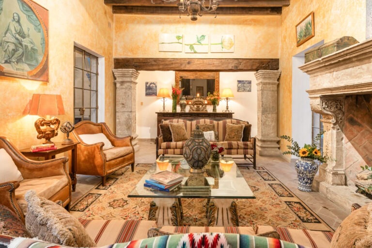 Warm living room with yellow plaster walls, wooden beams, and antique furniture around a glass coffee table, San Miguel de Allende