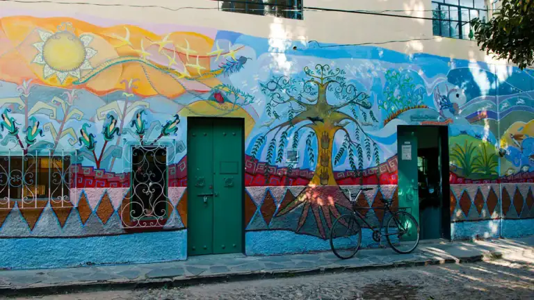 Colorful mural on a building with green doors, a bicycle parked outside, and stylized trees and hills in bright colors.