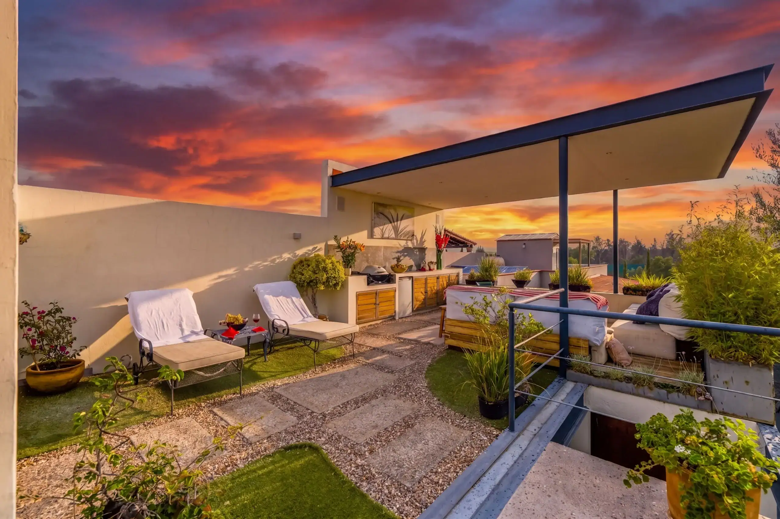 Rooftop terrace with white walls, cushioned lounge chairs, and potted plants under a vivid orange sunset sky, San Miguel de Allende