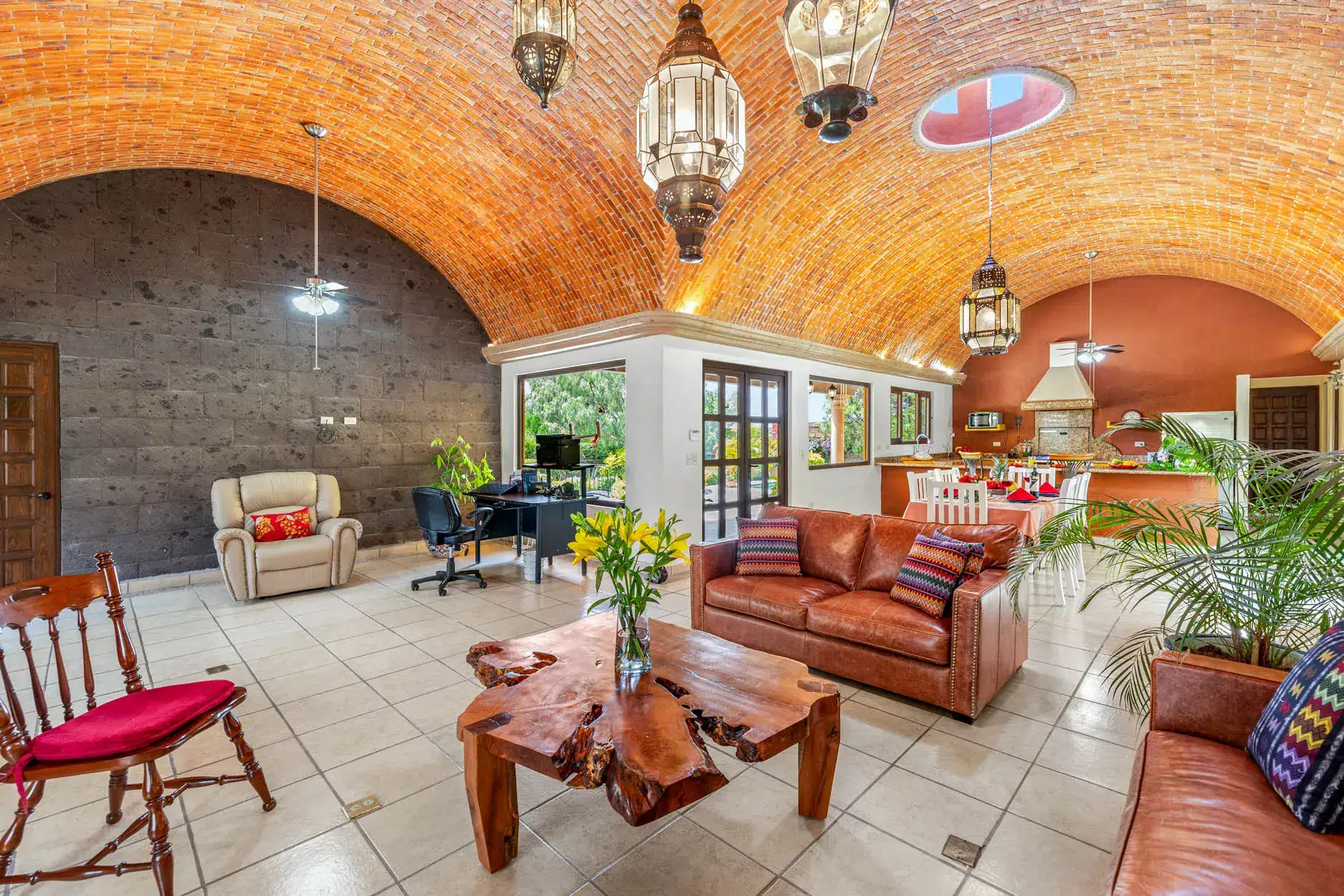 Open living area with a brick vaulted ceiling, leather sofa, and a natural wood coffee table, with a dining/kitchen area in the background, San Miguel de Allende