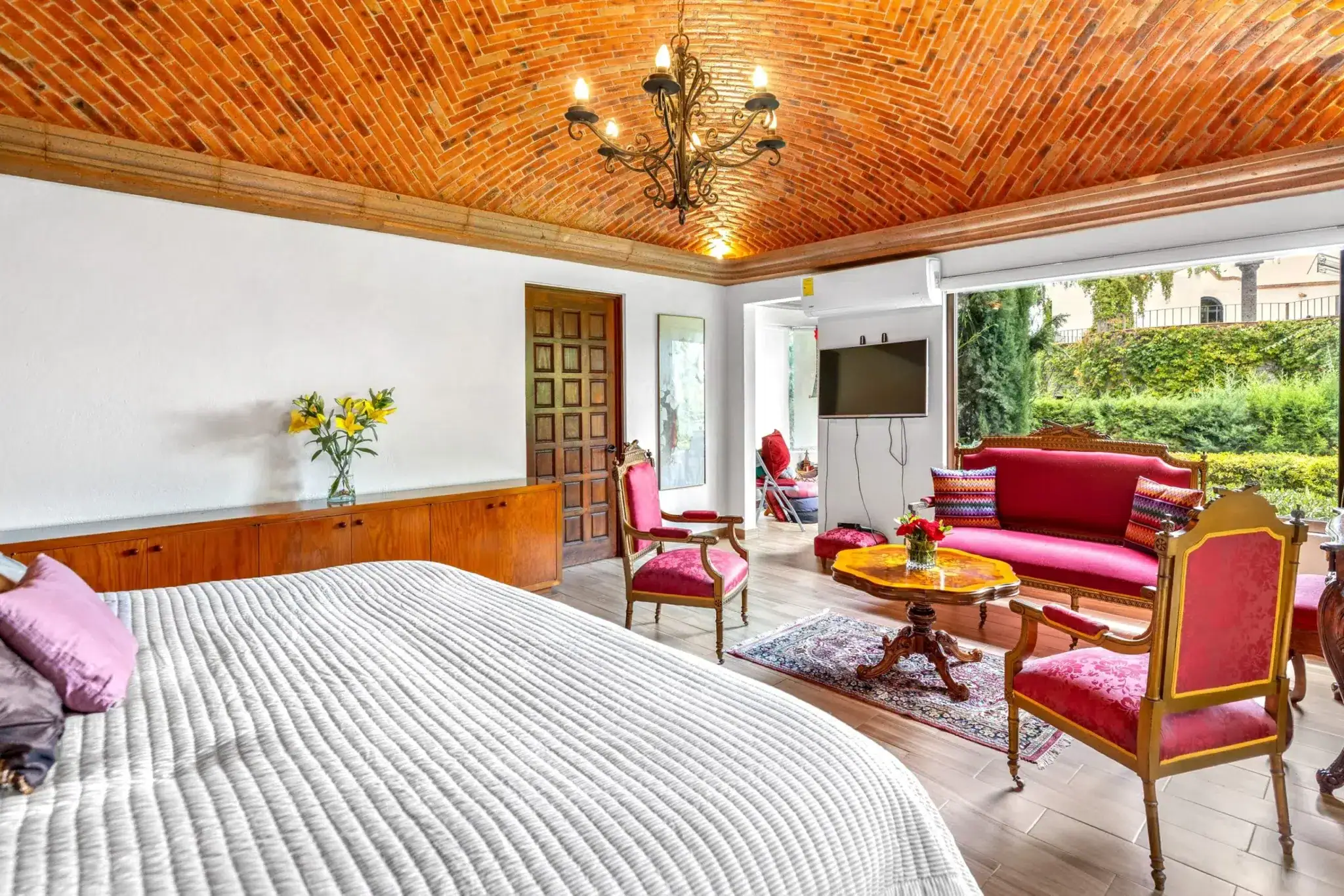Living room with a brick vaulted ceiling, chandelier, red upholstered furniture, and an open doorway to a garden view, San Miguel de Allende