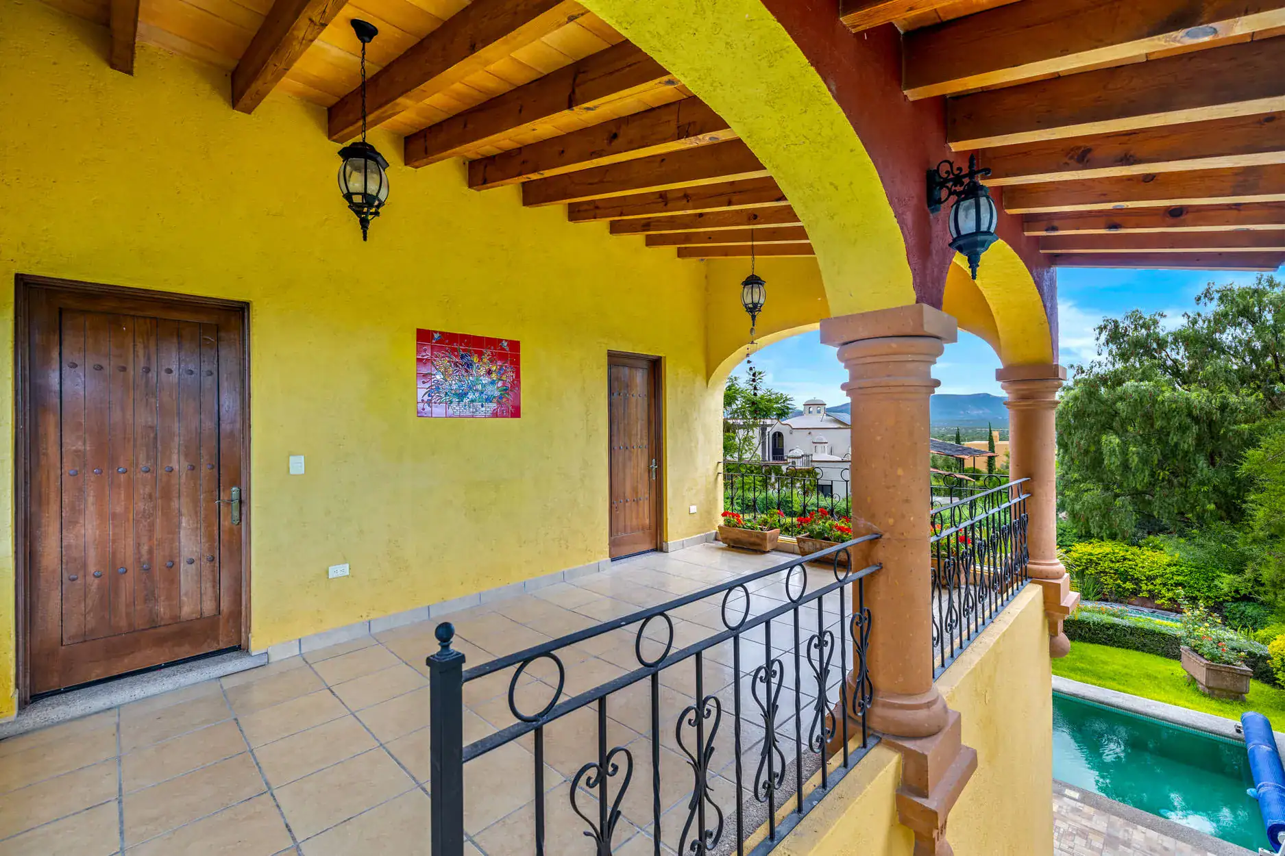 Mediterranean-style veranda: yellow walls, wooden doors, decorative arches, lanterns, and a black wrought-iron railing, San Miguel de Allende