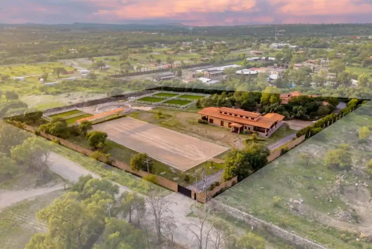 Aerial view of a small town with sports fields, fenced arenas, and tree-lined streets at sunset/light haze, San Miguel de Allende