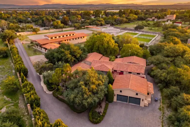 Aerial view of a suburban ranch area with terracotta roof buildings, white fencing, riding arenas, and sunset lighting, San Miguel de Allende