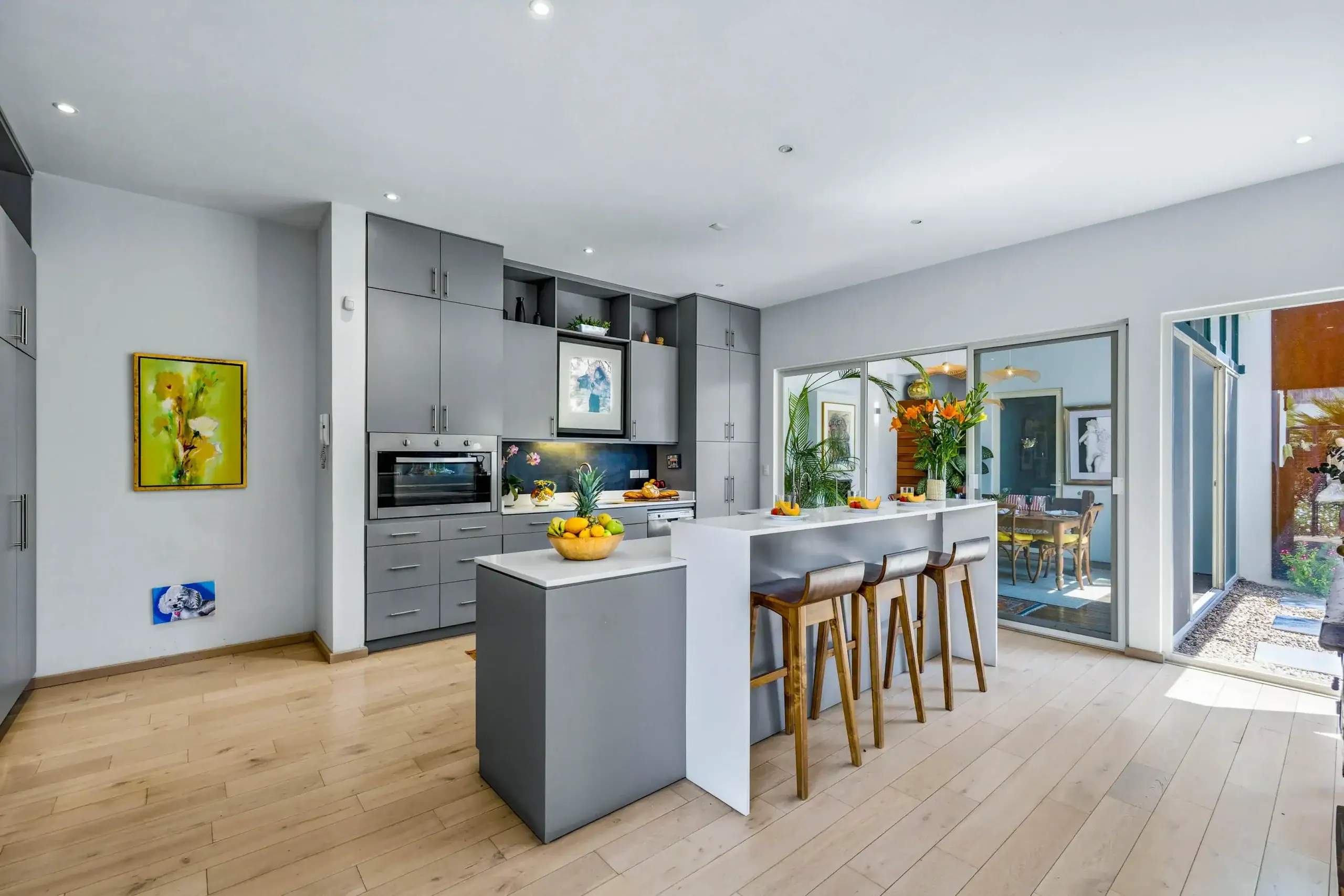 Modern gray kitchen with island and bar stools, open to a sunlit dining area through sliding glass doors to the yard, San Miguel de Allende