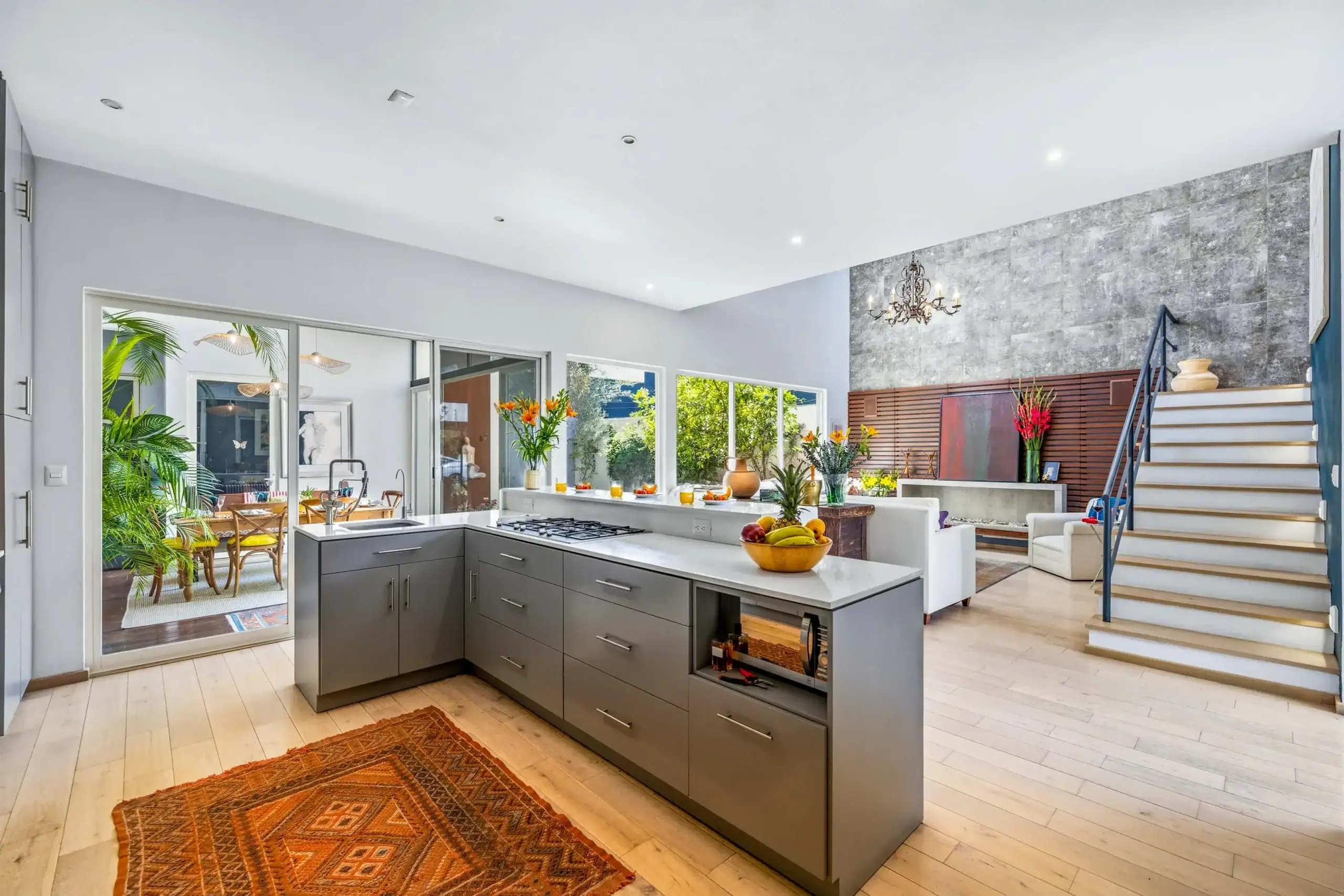 Open-concept kitchen with gray cabinets, white countertops, an island, and a fruit bowl; glass doors lead to a dining area and plants sit nearby, San Miguel de Allende