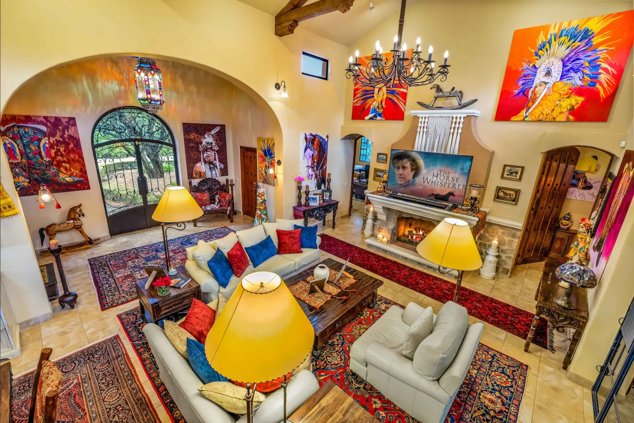 Bohemian living room with cream sofas, yellow lamps, and vibrant wall art including large colorful portraits and a chandelier, San Miguel de Allende