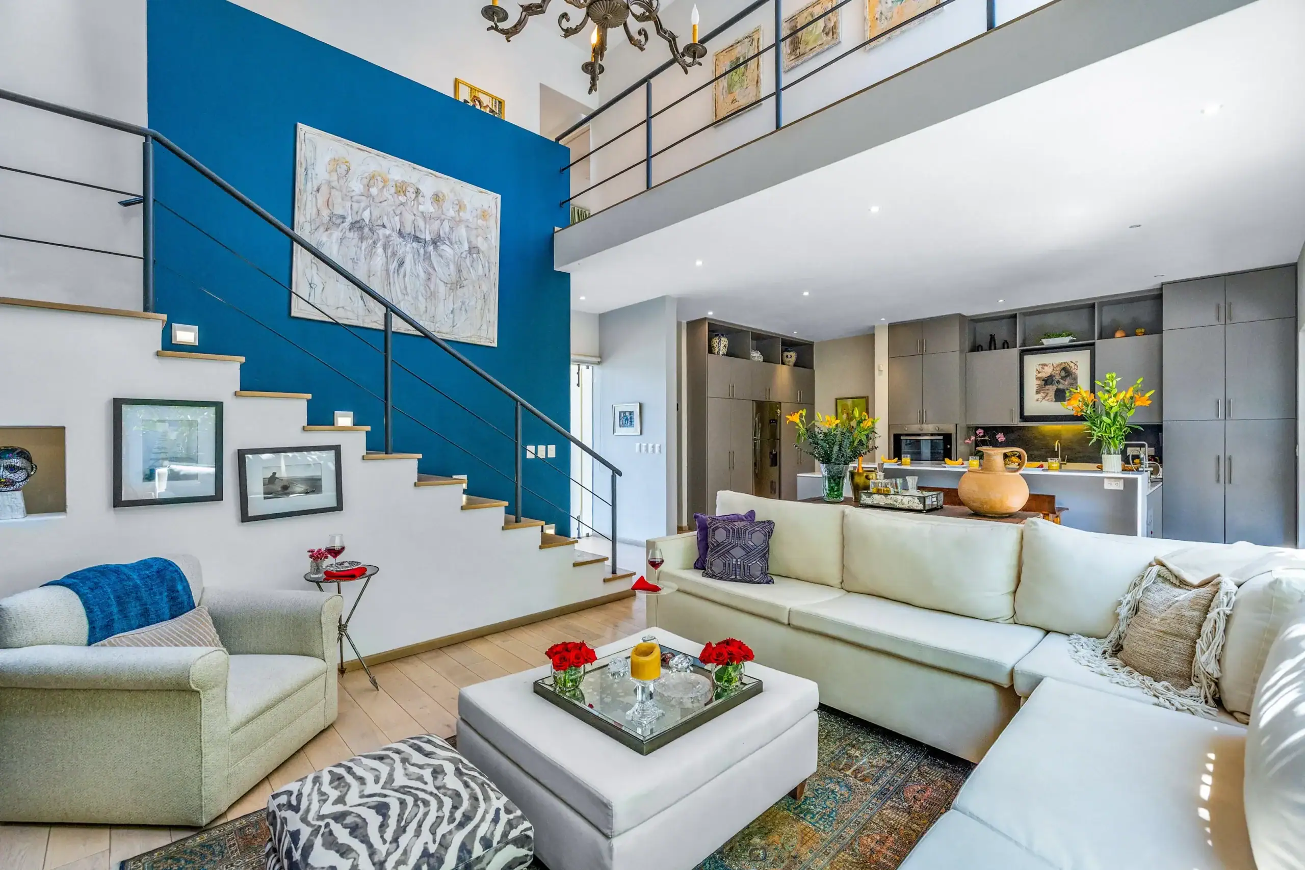 Open-concept living room with a blue accent wall, gray sectional sofas, and a glass-topped coffee table facing a modern kitchen, San Miguel de Allende