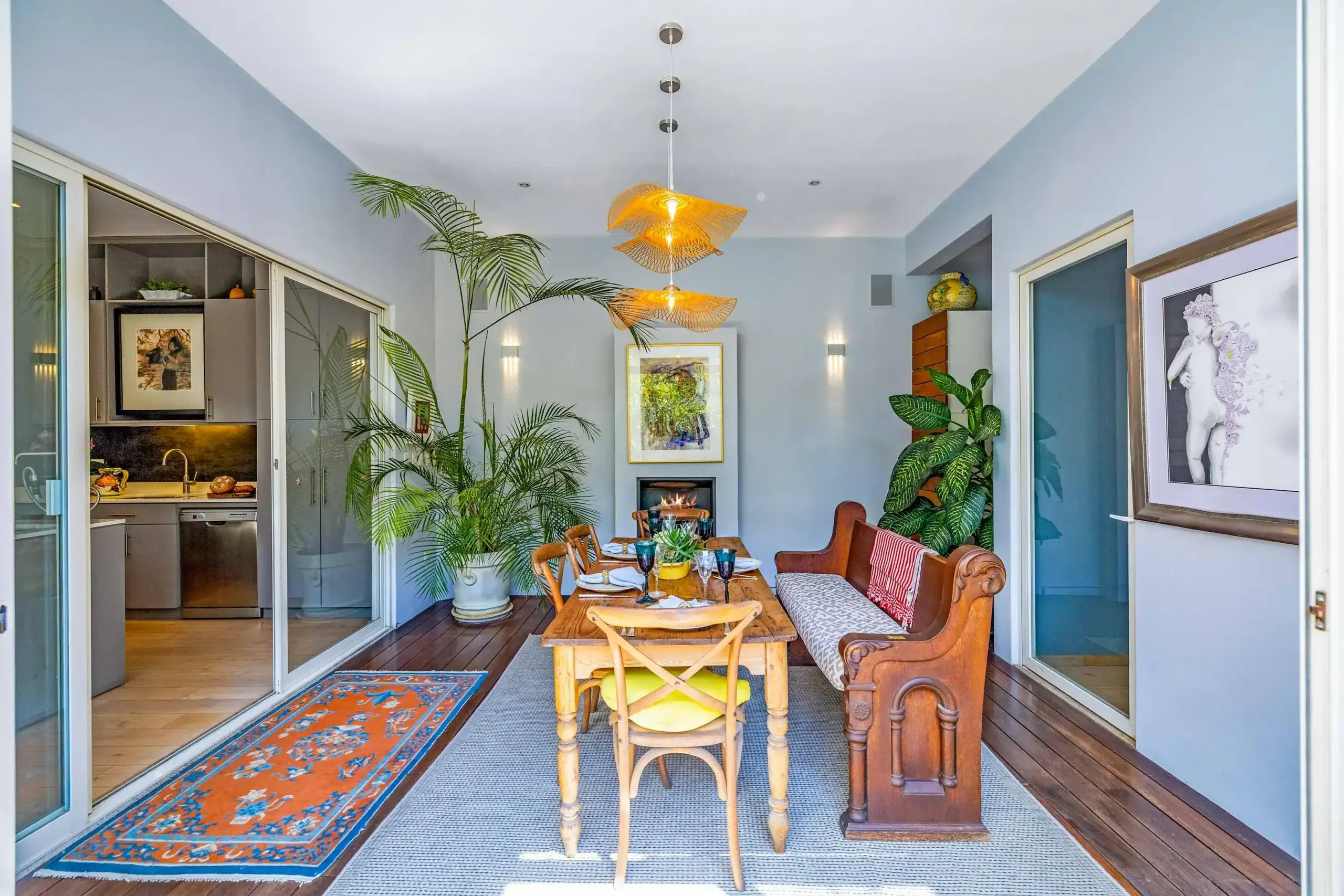 Open‑plan dining area on a covered patio with a wooden table set for a meal, surrounded by tall tropical plants and woven pendant lights, San Miguel de Allende