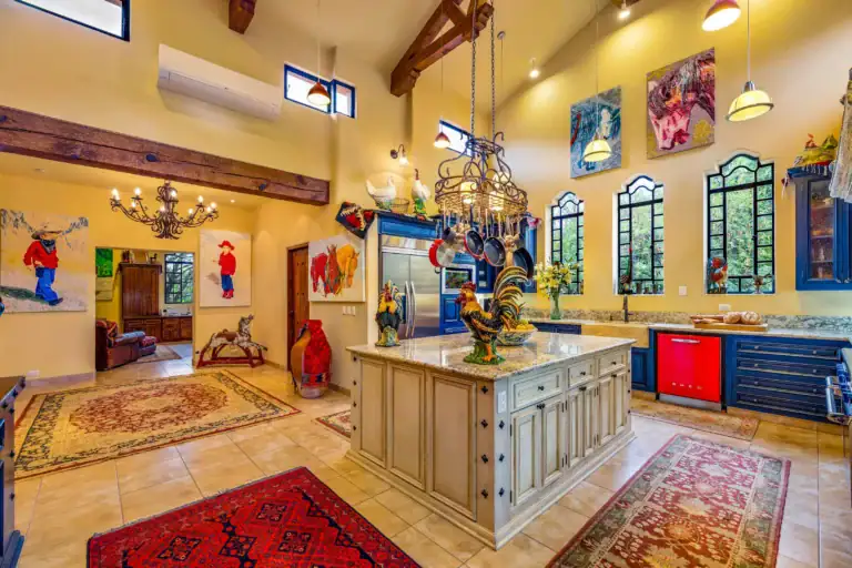 Bright country kitchen with yellow walls, exposed wooden beams, hanging pot rack, and blue cabinets at the island area, San Miguel de Allende